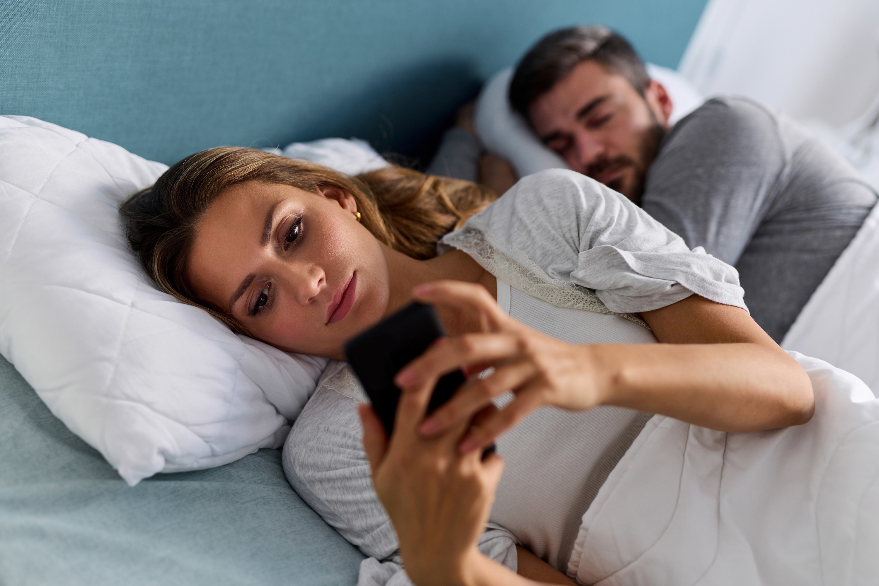 A woman with her back to her partner in bed while on the phone