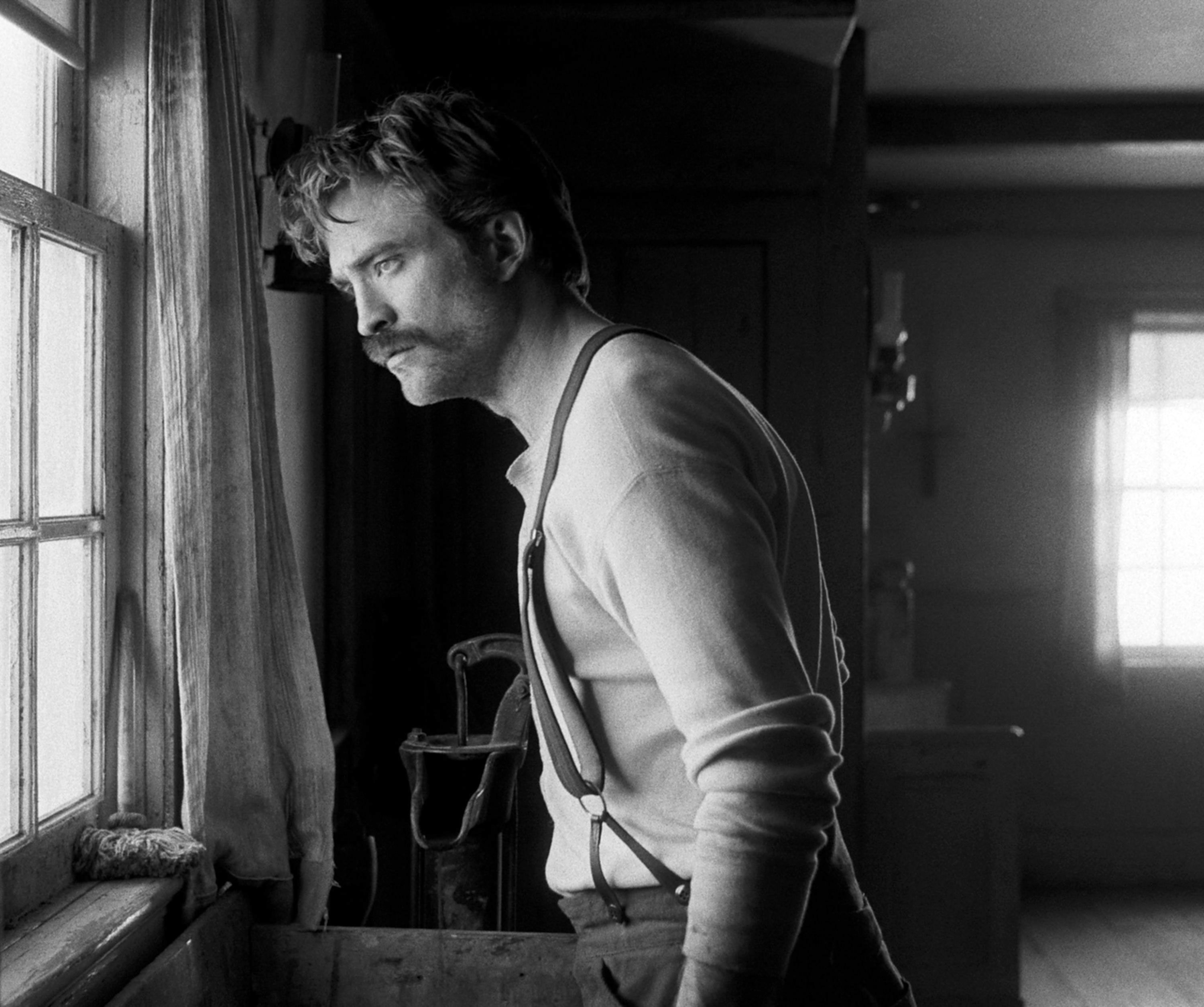 Black-and-white image of Robert with a mustache, wearing suspenders, and looking out a window