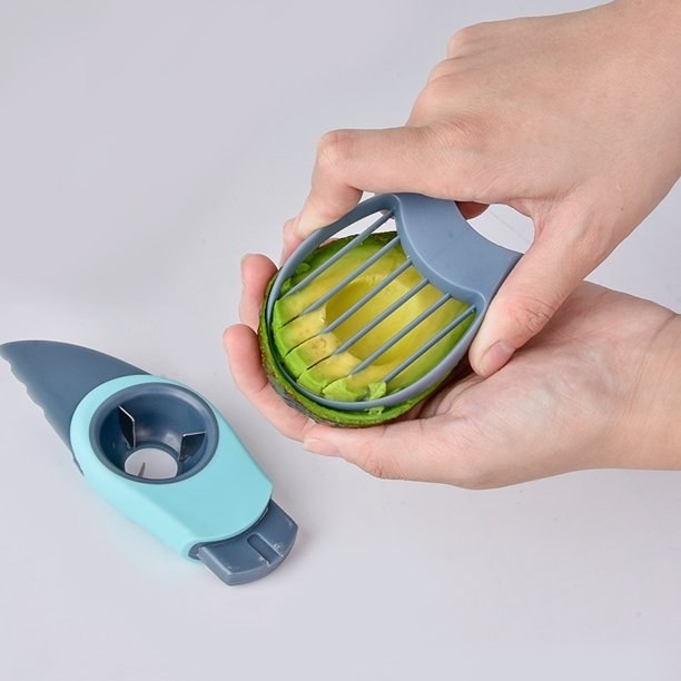 The tool being used to slice half an avocado