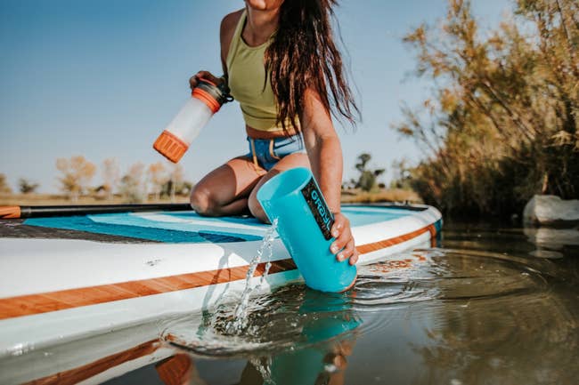 a model on a stand up paddle board getting water from a river or lake in the bottle