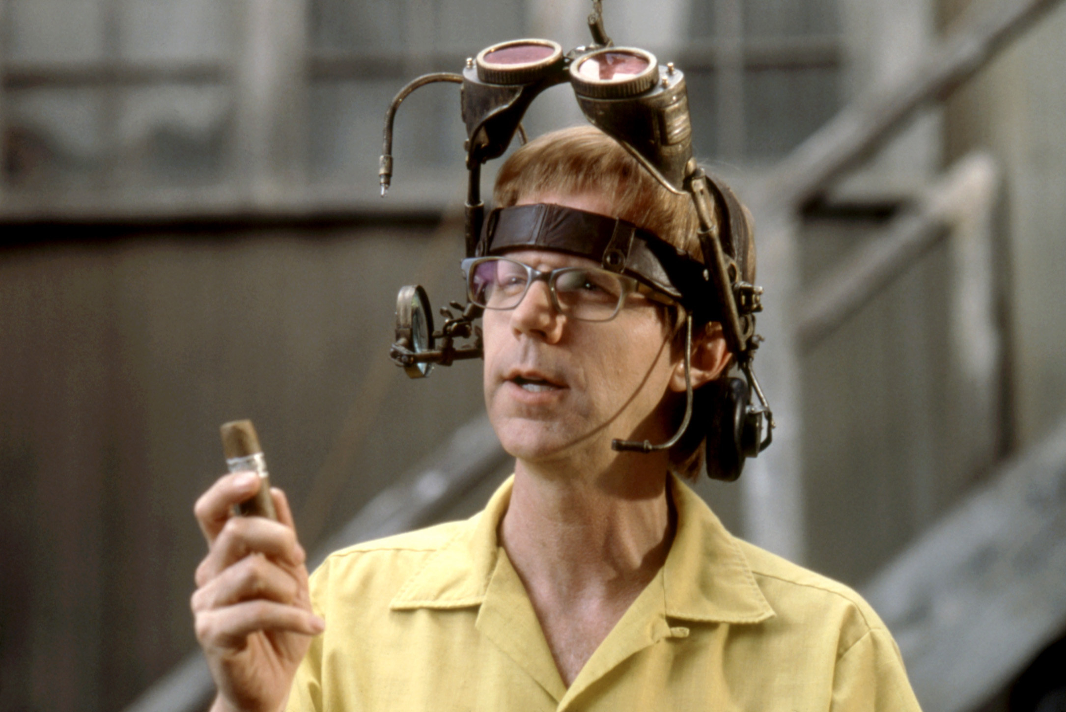 Dana Carvey wearing weird goggles and holding a cigar thinking