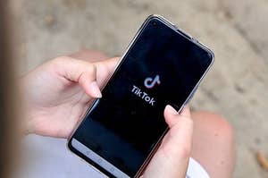 A pair of hands holds a smartphone with the TikTok app loading on the screen.