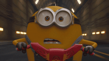 a gif of a minion with braces racing on a bicycle