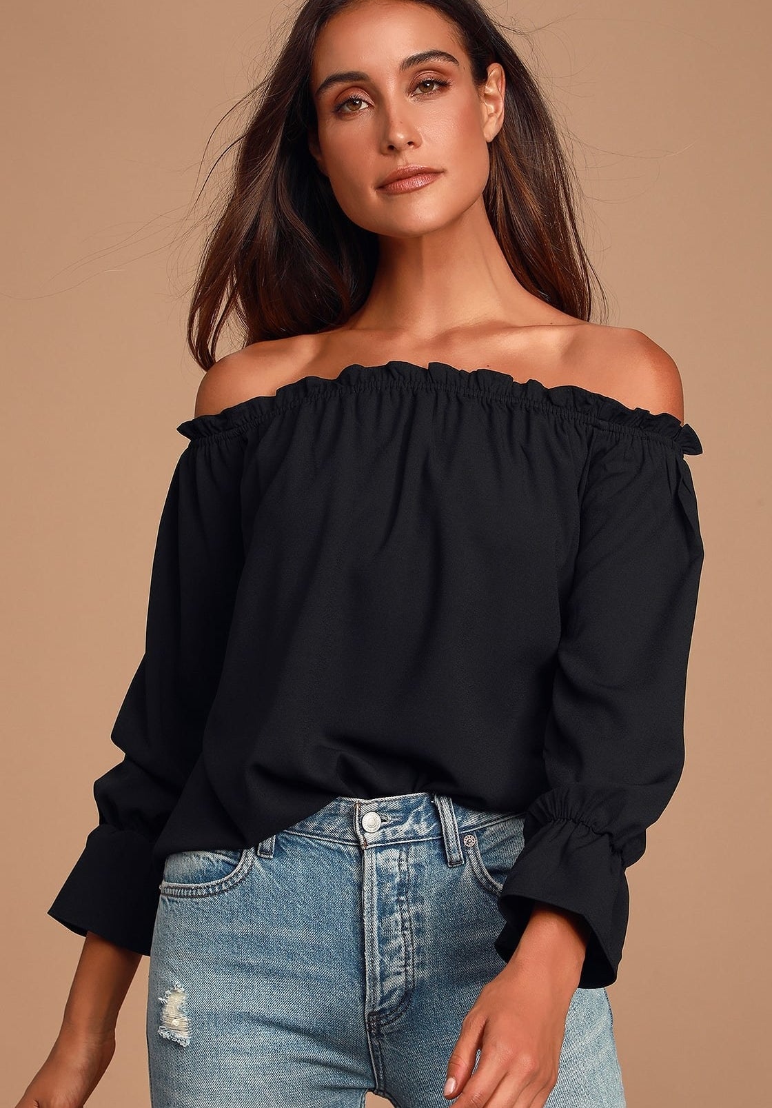 Model is wearing a black smocked off the shoulder top with denim jeans