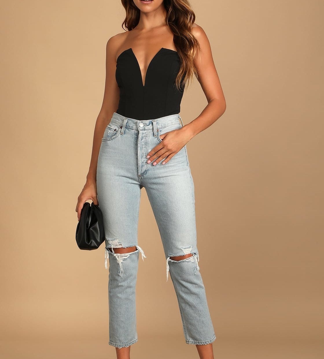 Model is wearing a strapless black bodysuit and denim jeans