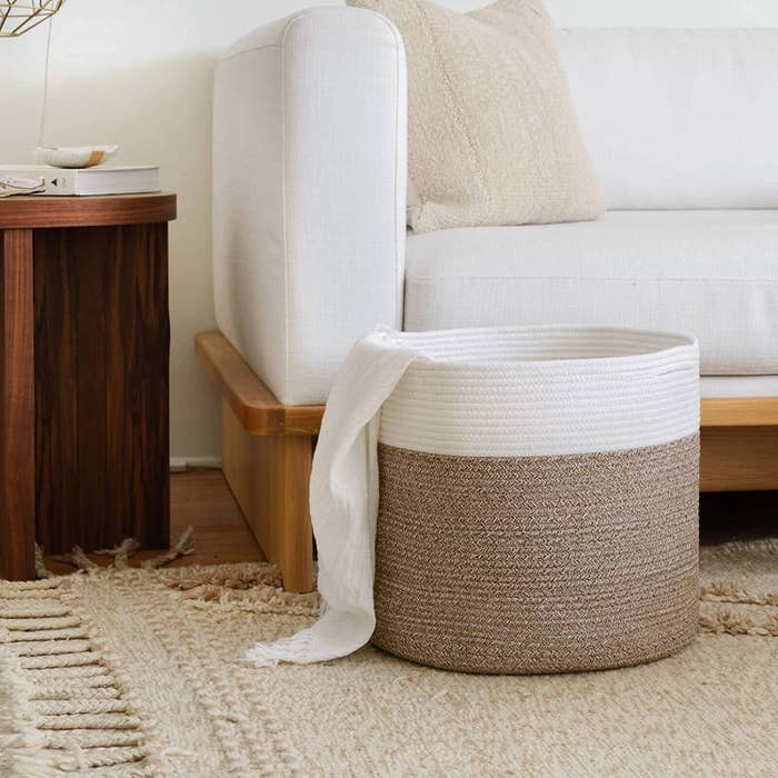 a woven basket in a living room with a throw blanket hanging out of it