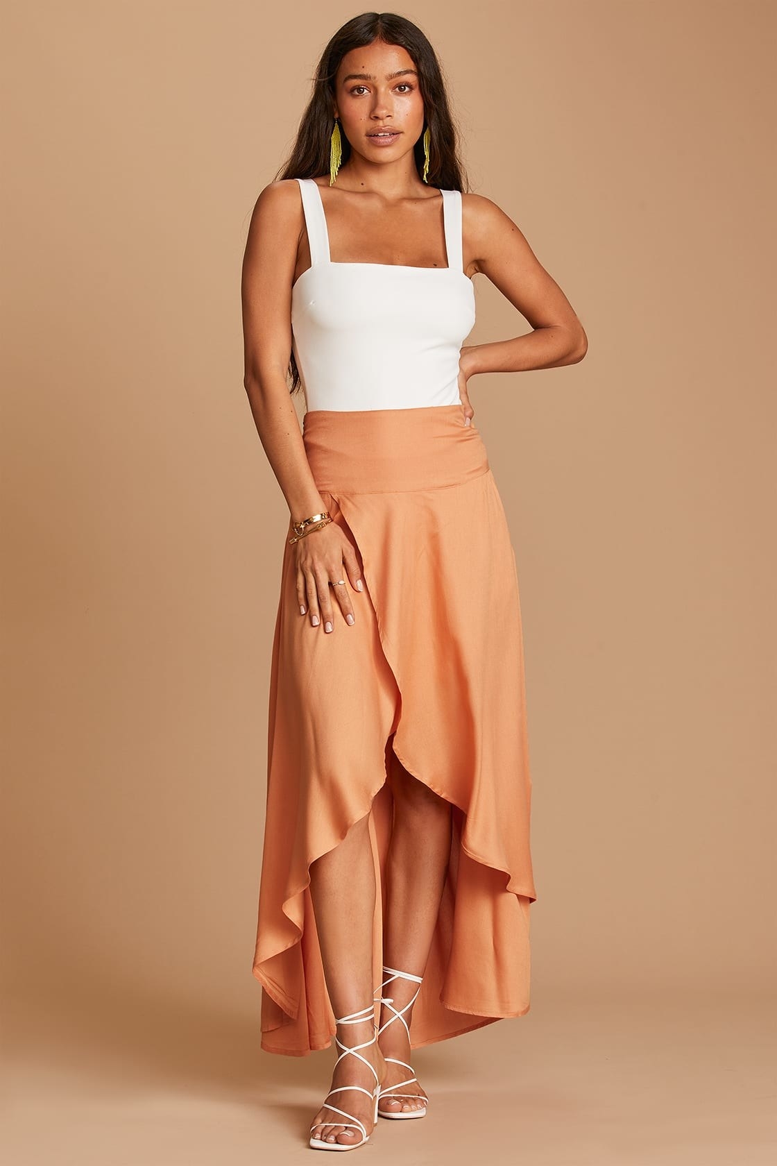 Model is wearing a white top and light orange maxi skirt with white sandals