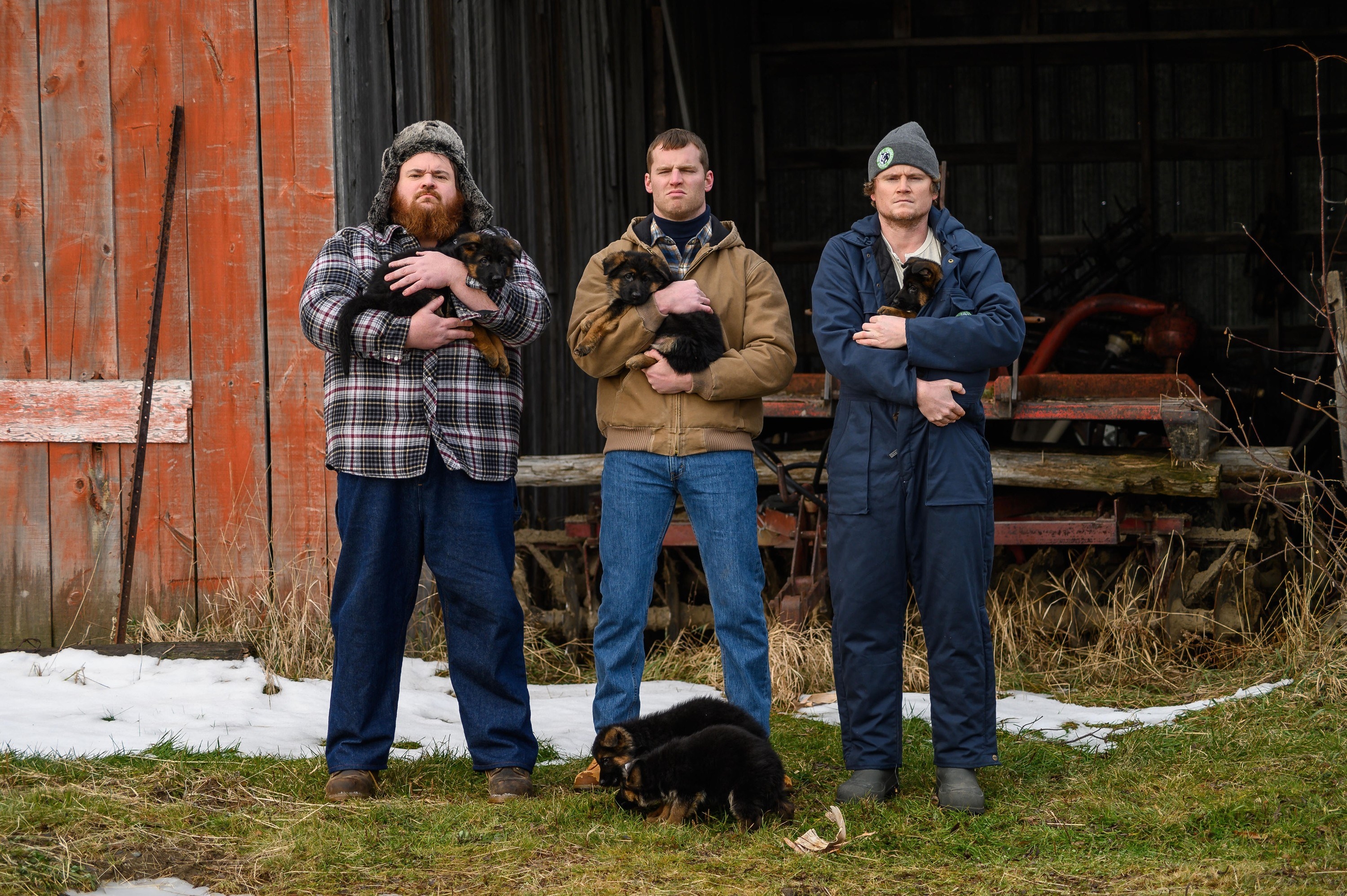 Three guys holding puppies outside a barn