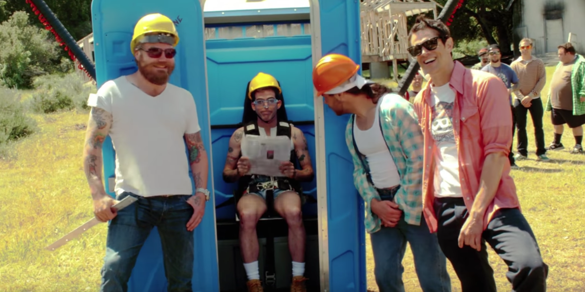 the cast of jackass standing by a portable toilet