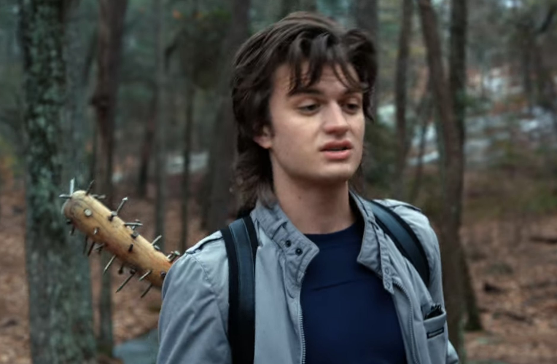 Steve walks in the woods, a baseball bat with nails in hanging out of his backpack