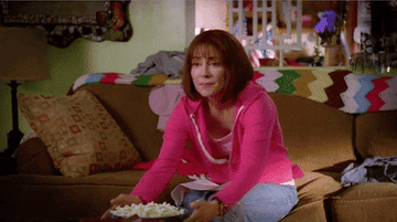 Woman sitting on a couch and grabbing a bowl of popcorn
