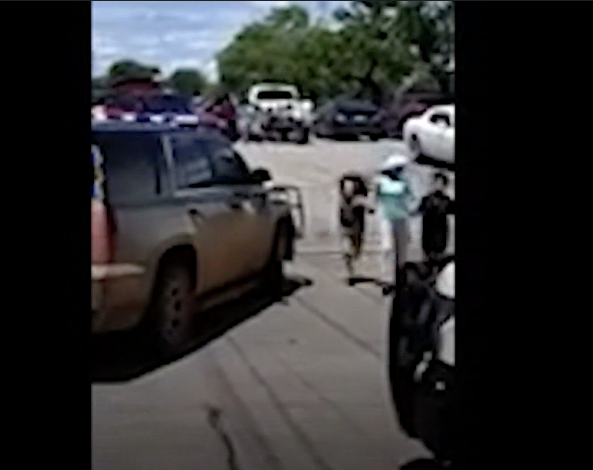 Screenshot of someone wearing a hat and holding two children&#x27;s hands near cars in a parking lot
