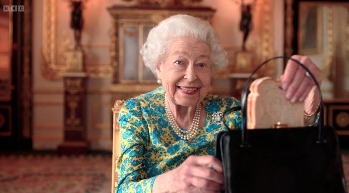 The Queen smiling as she takes a sandwich out of her handbag