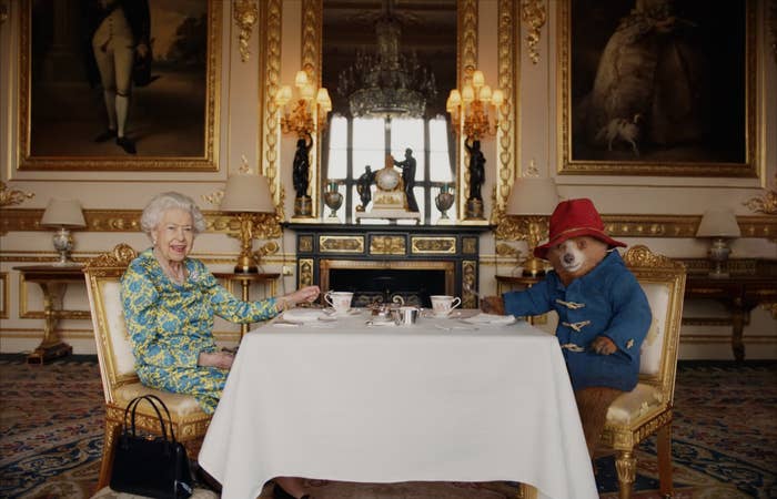 The Queen, with her handbag on the floor by her chair, and Paddington Bear sitting at a table together