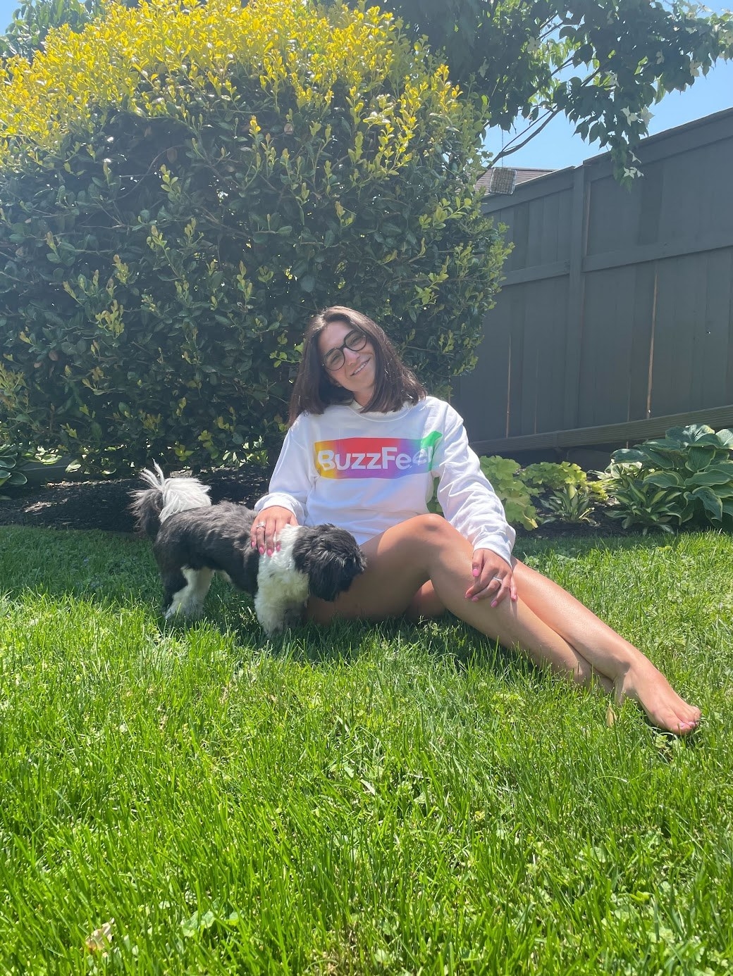 Model wearing sweatshirt sitting in the grass petting a dog