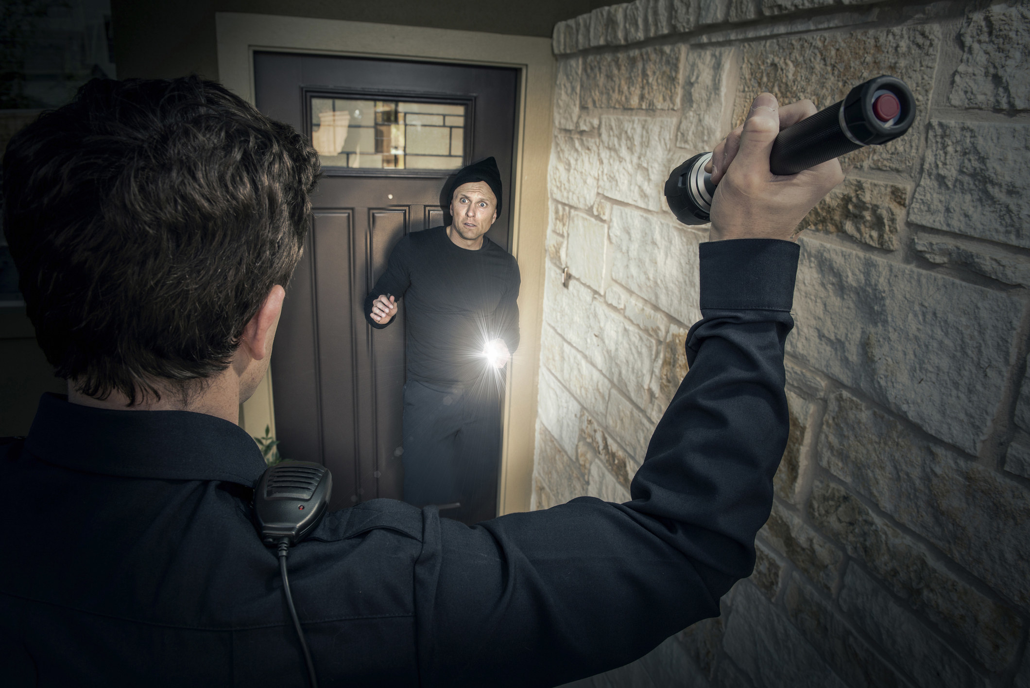 a cop shining a flashlight at someone trying to get in through the front door