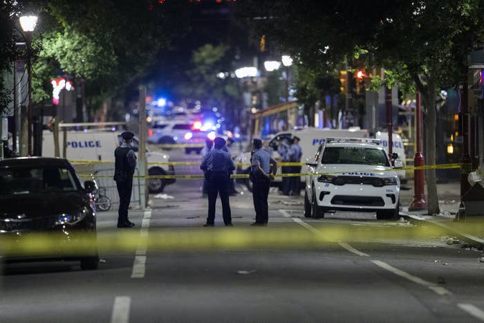 Police stand behind police lines on a street with police cars and other cars