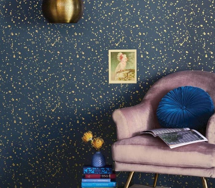 Gold and navy celestial wallpaper with velvet chair in the foreground