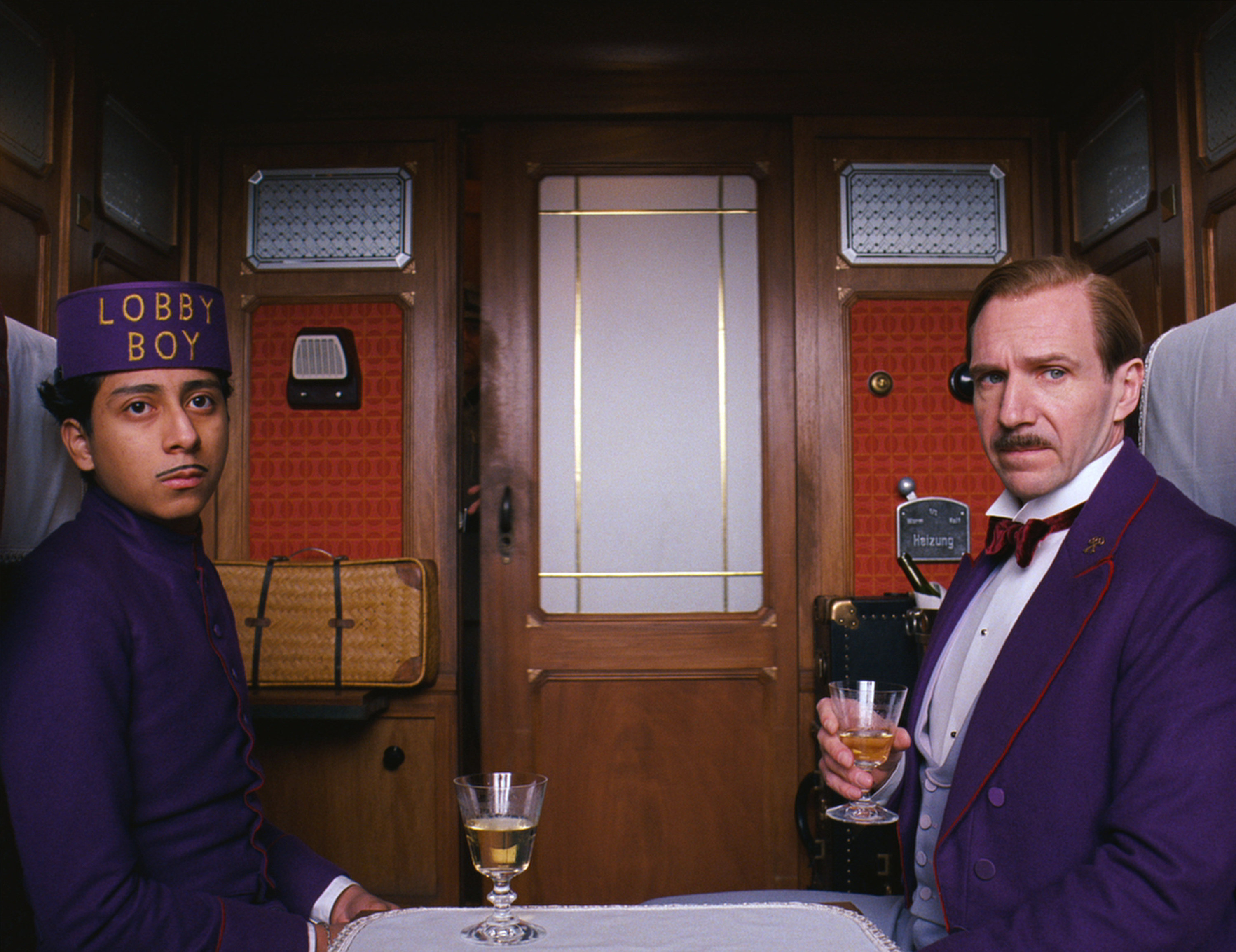 Ralph Fiennes and Tony Revolori  on a train in their hotel uniforms in the grand budapest hotel