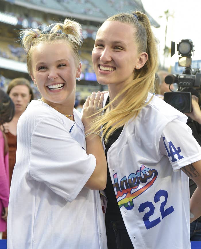 JoJo and Kylie at a baseball game wearing Dodgers jerseys; Kylie&#x27;s jersey has the team name designed in the colors of the Pride flag