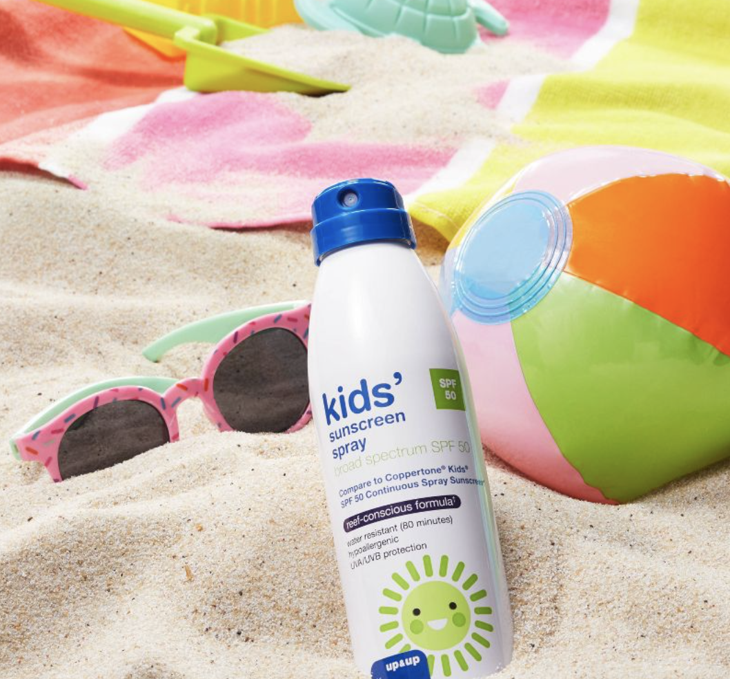 A bottle of kid&#x27;s sunscreen in the sand with sunglasses and a beach ball