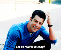 a gif of schmidt from new girl saying let us rejoice in song