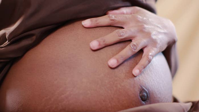 A close-up of a Black, pregnant woman&#x27;s stomach with her fingers splayed out on the bump