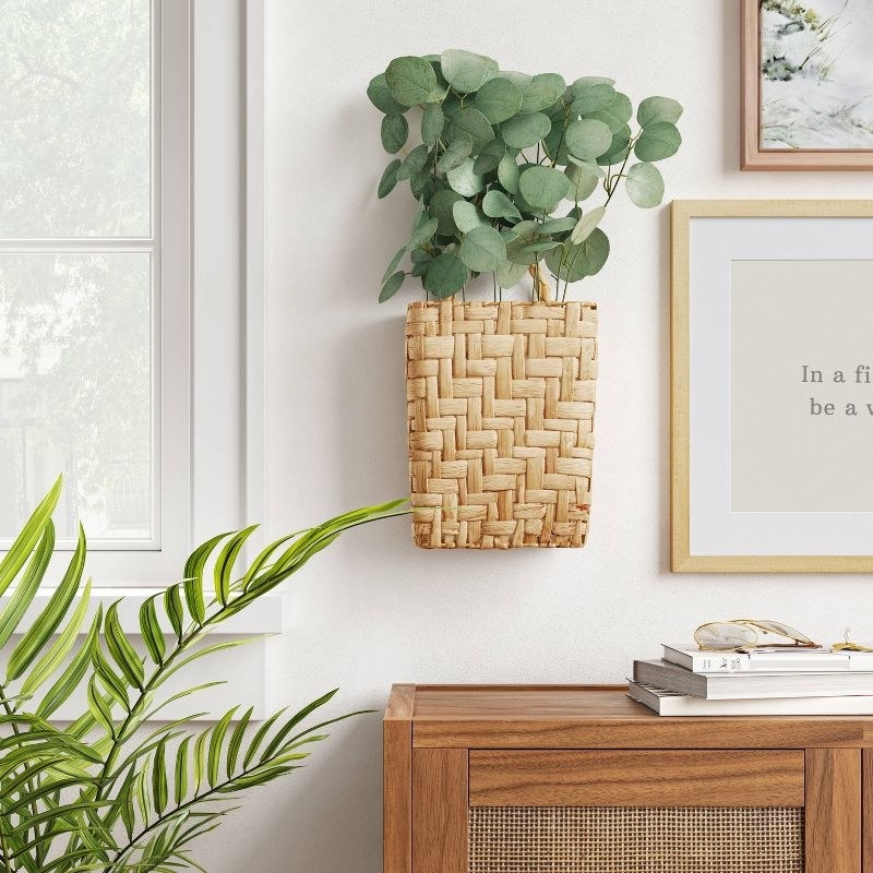 An image of a hanging woven planter with faux eucalyptus plants