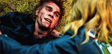 Archie lying on the ground, bloodied and smiling, as Betty touches his face