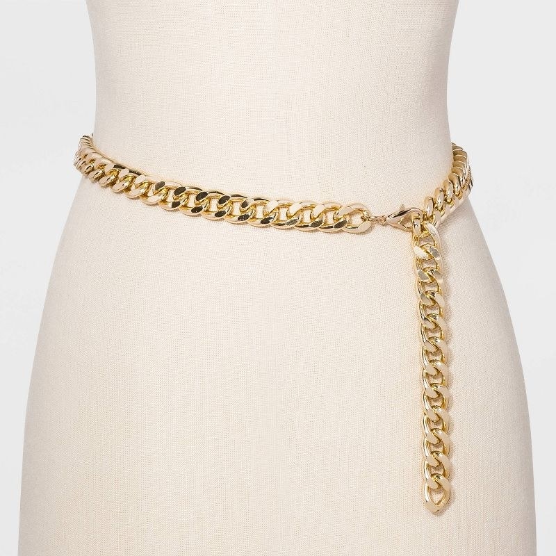 The gold chain belt is draped around a mannequin waist