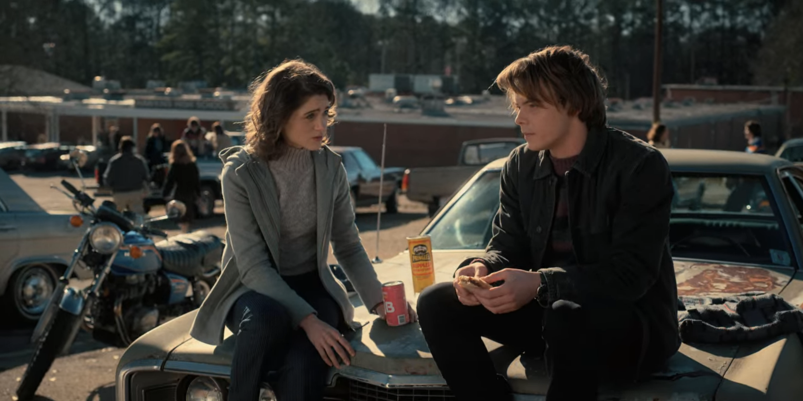 sitting on a car, Nancy wears jeans and a gray turtleneck sweater under a gray jacket