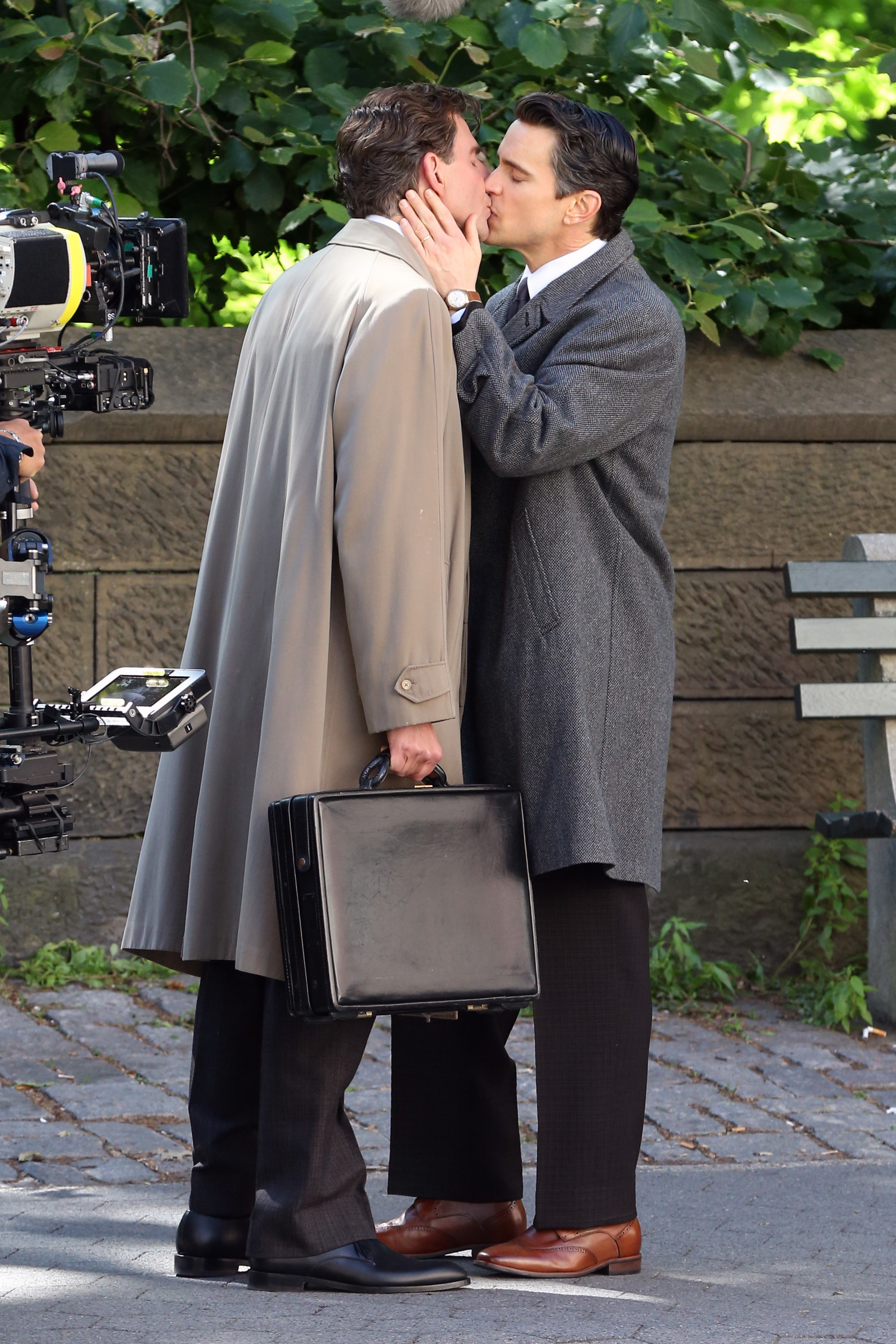 Matt holds Bradley&#x27;s face as they kiss while standing on a sidewalk and Bradley holds a briefcase