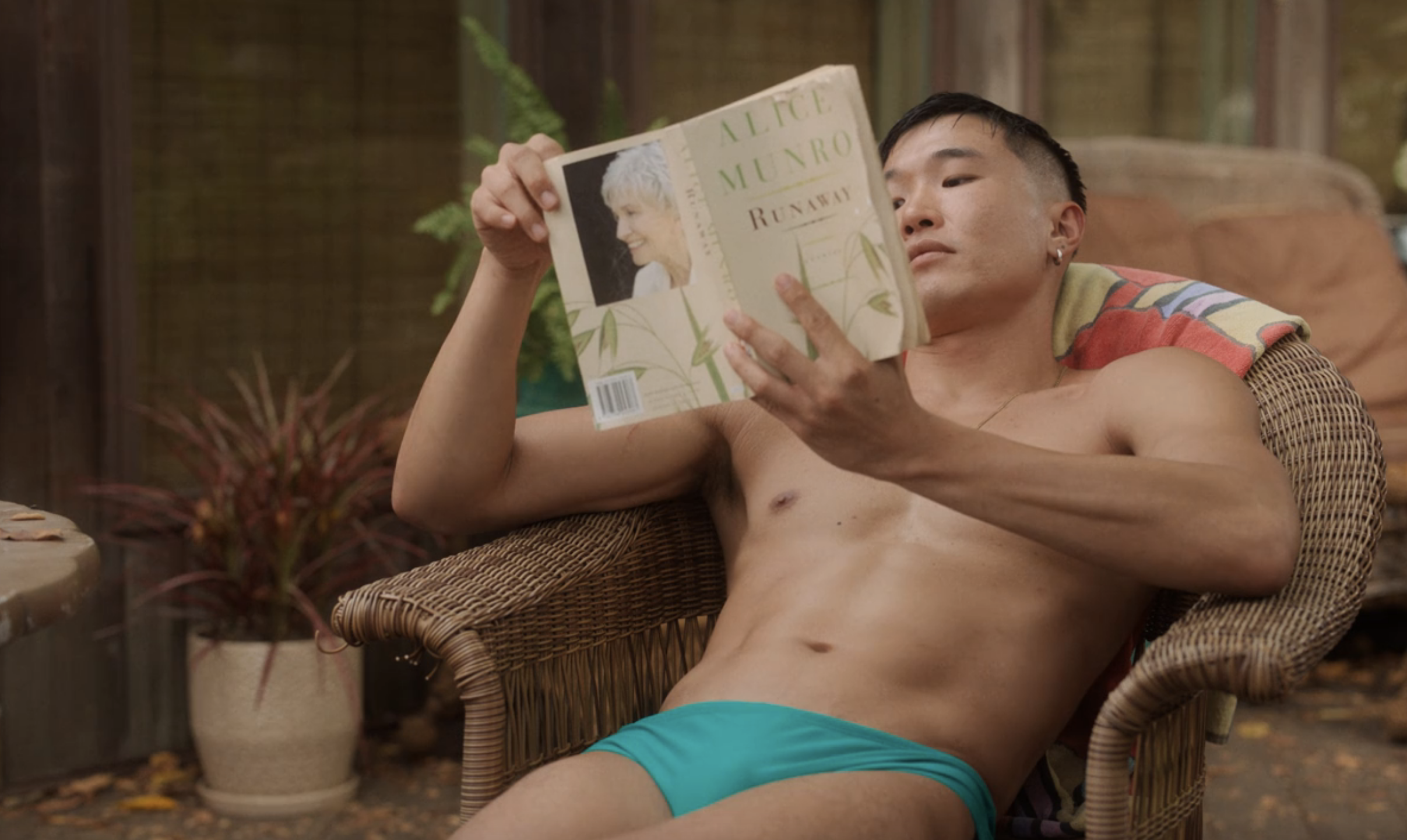 A man in briefs relaxing in a chair and reading Runaway by Alice Munro