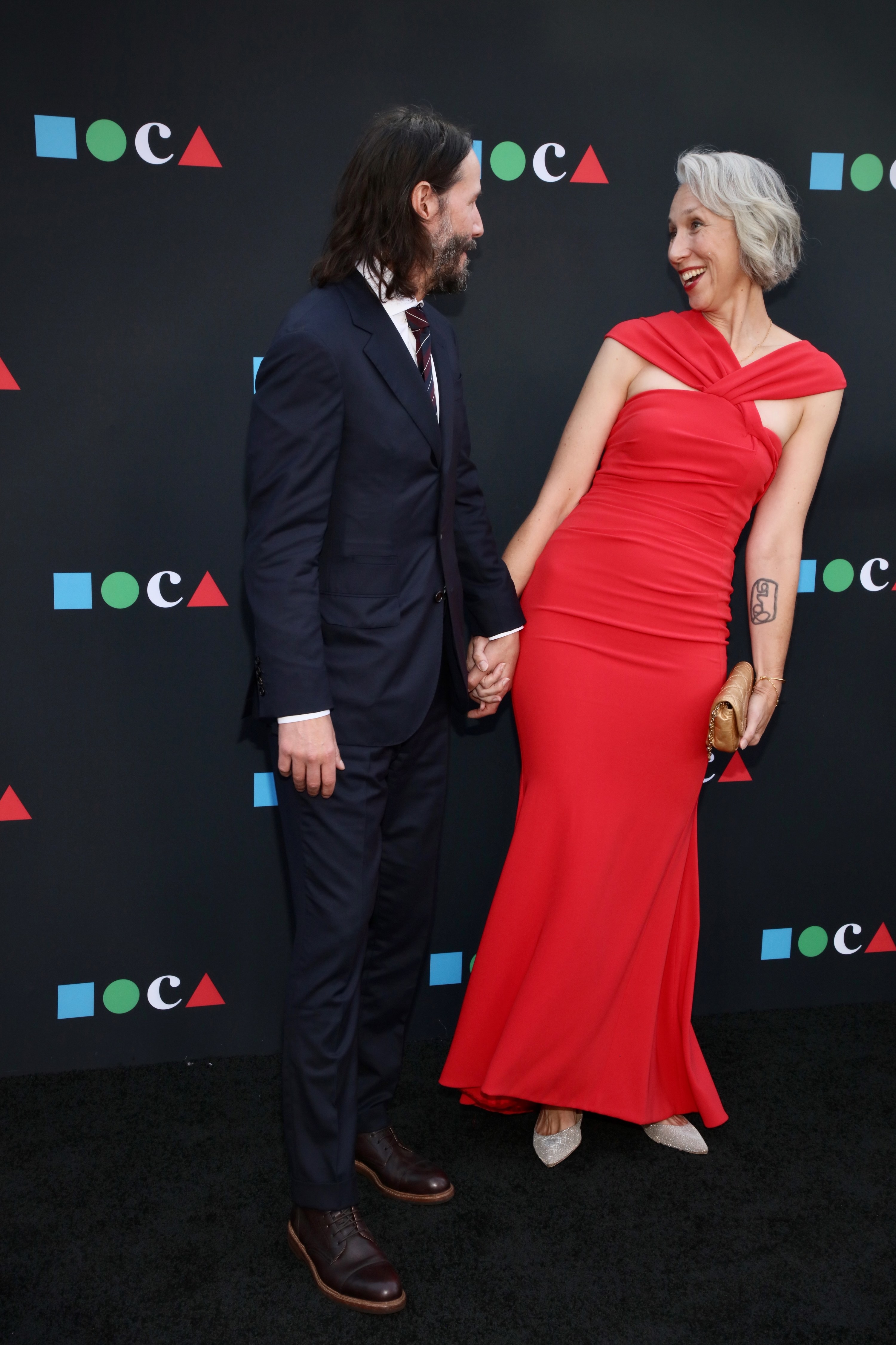 Keanu and Alexandra grin while holding hands