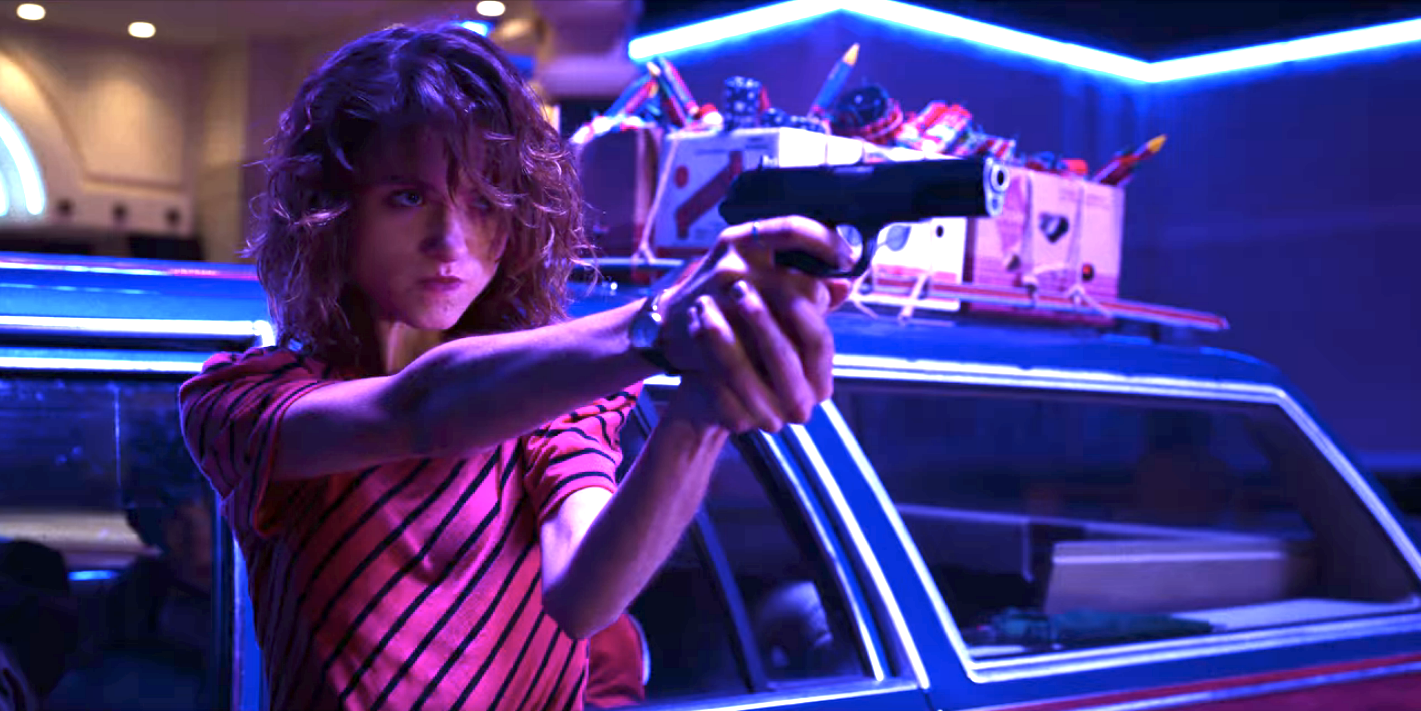 Nancy pointing a gun while leaning out the car window wearing a diagonally striped top