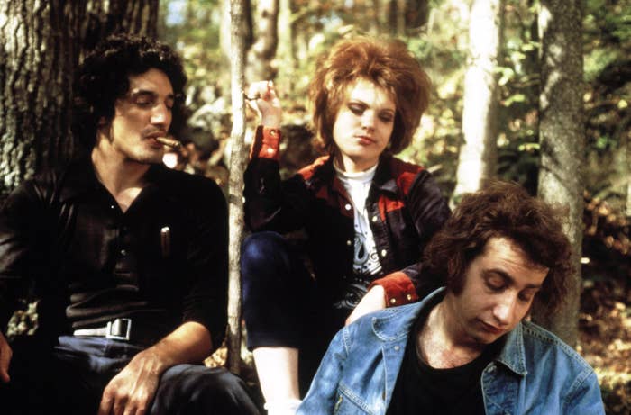 A group of two men and a woman, looking sinister, sit smoking on a forest floor