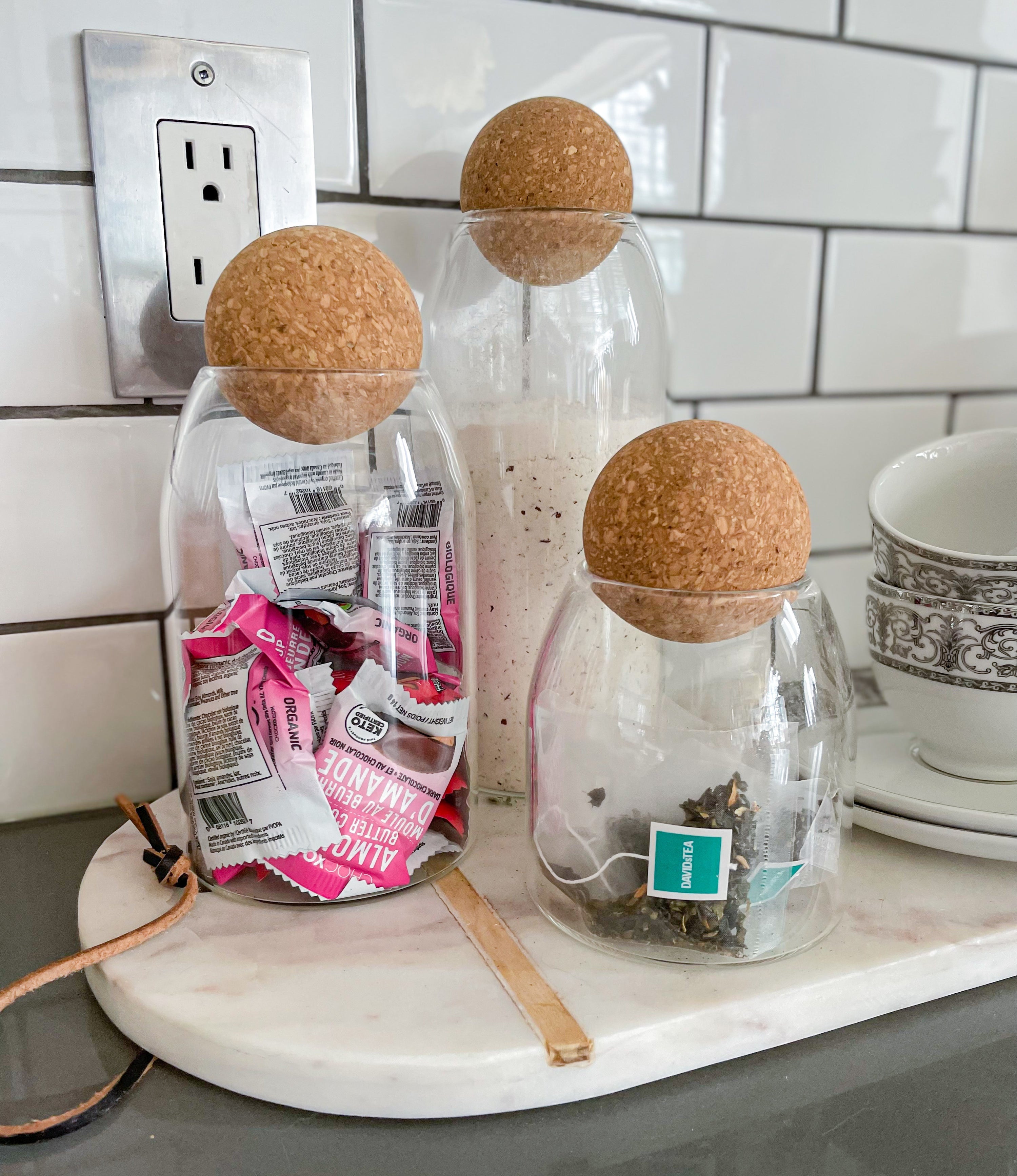 a trio of glass canisters with cork ball tops filled with tea and snacks