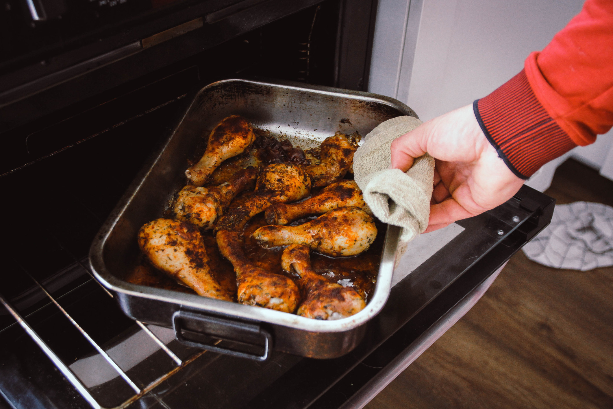 Hands getting a roasting tray of chicken out of the oven