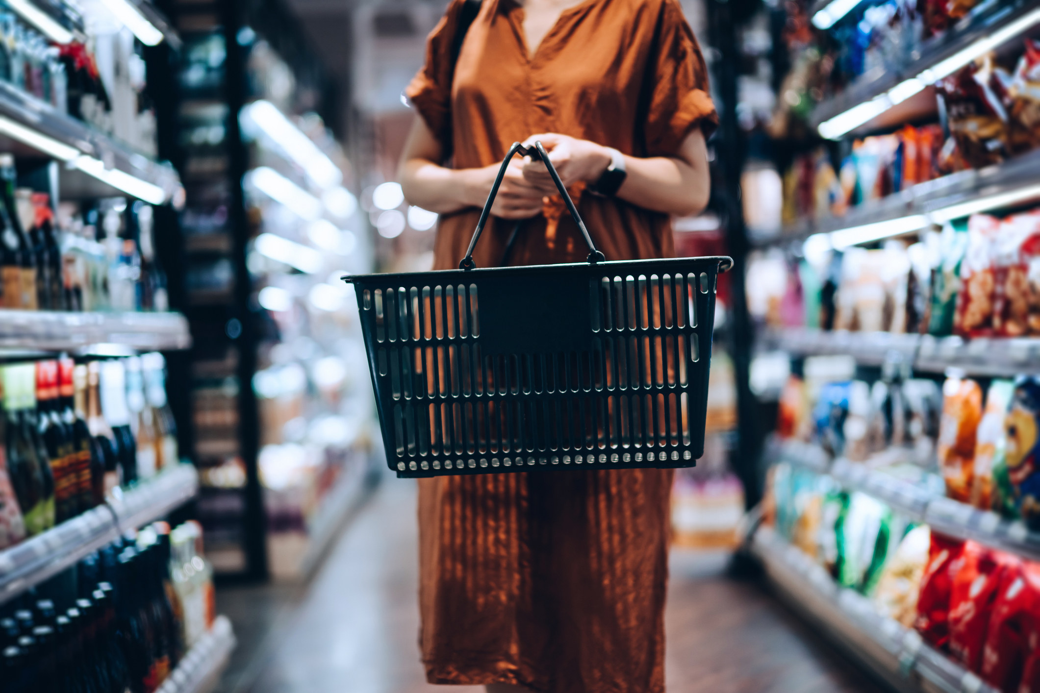 A young woman carrying a shopping basket in a grocery store