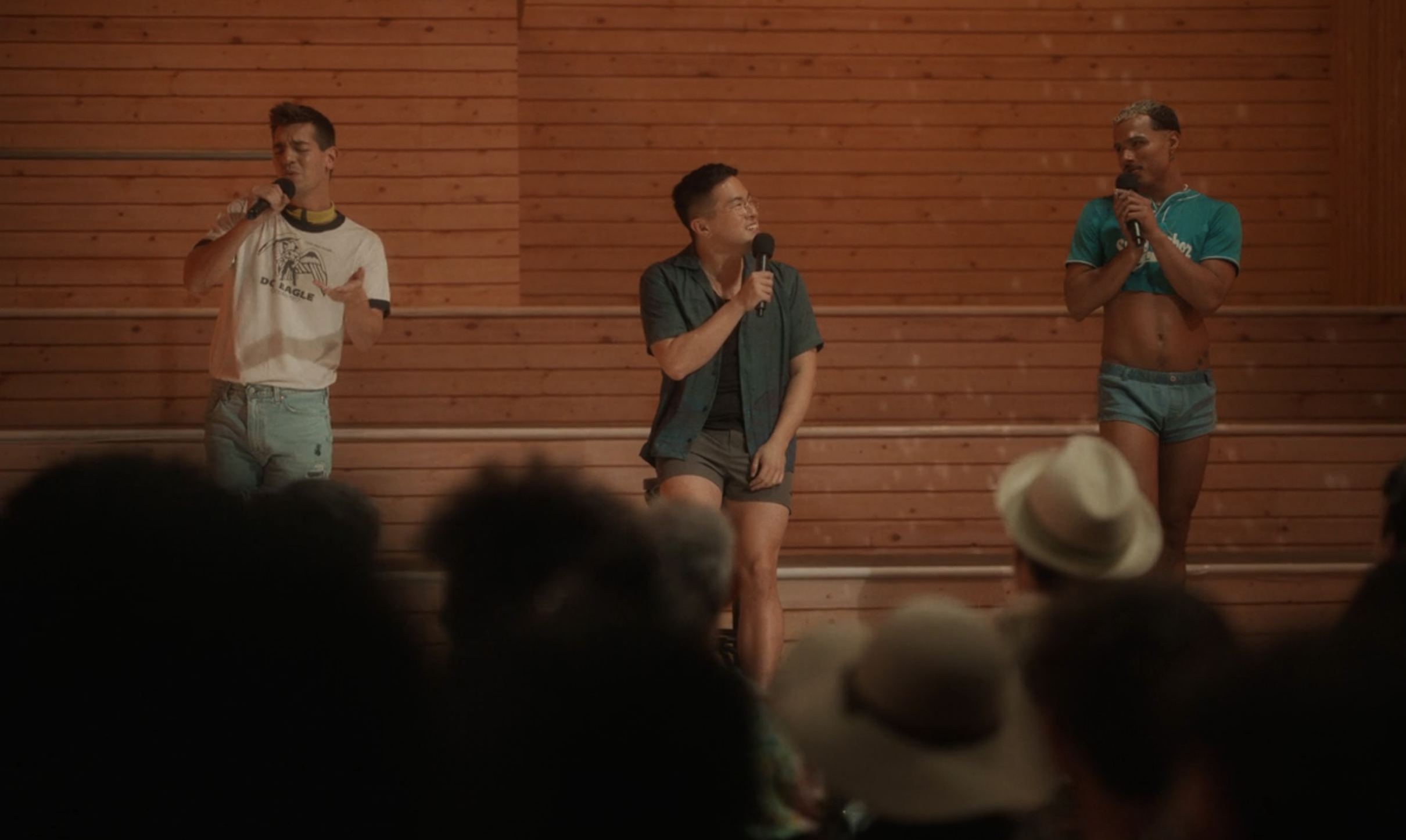 Three men, two of them wearing shorts, singing into microphones