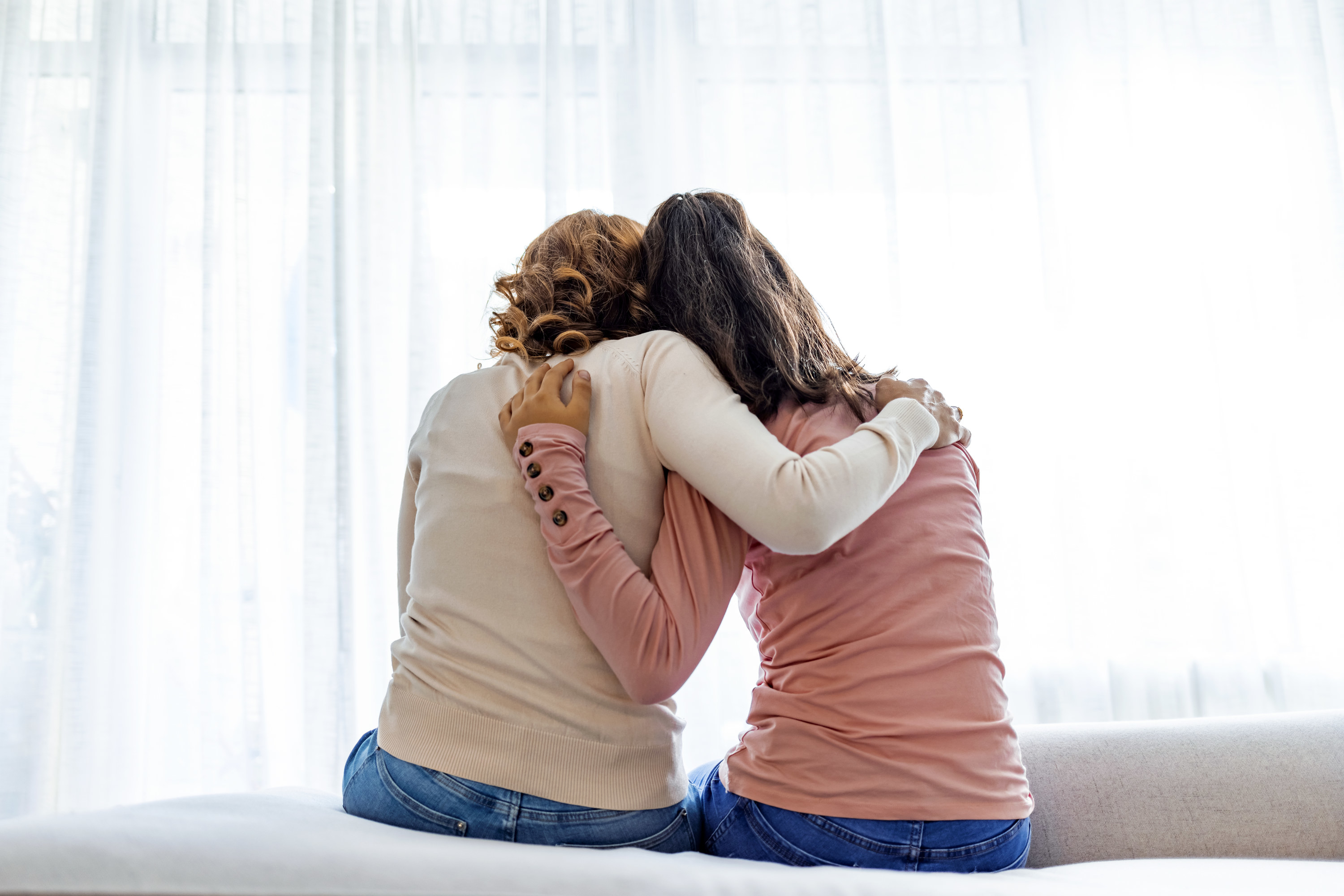 A mom and her daughter are shown from behind as they hug each other