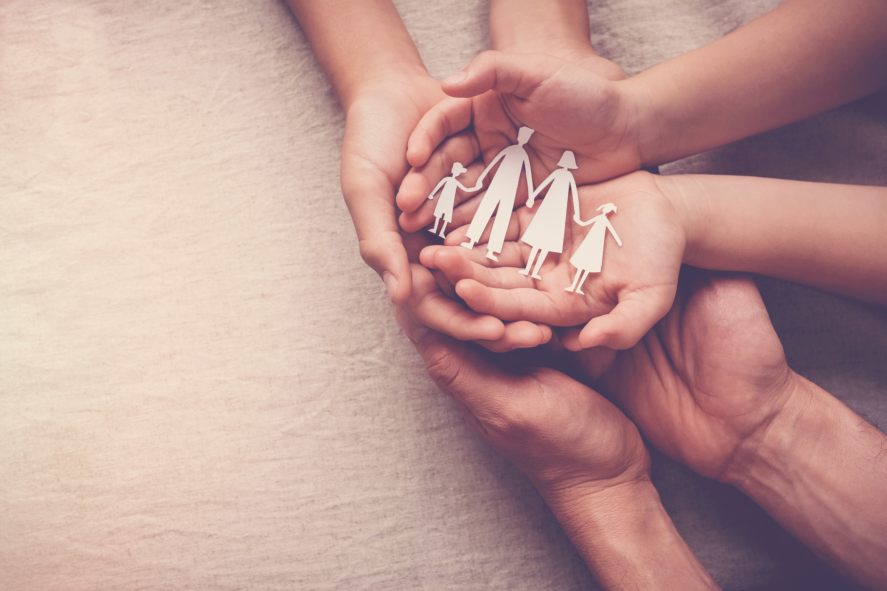 Hands of a parent and children together hold a paper cutout of a family