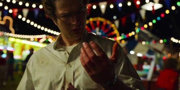 A bespectacled man stares shockingly at his hand. He is attending a fair