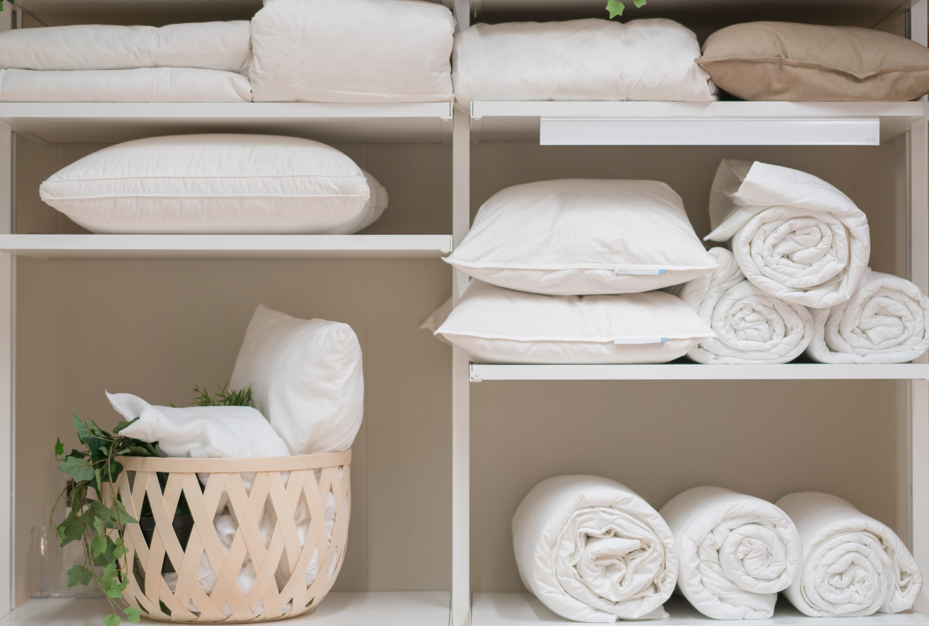 Various household items such as pillows and quilts standing in the white cupboard in the laundry room