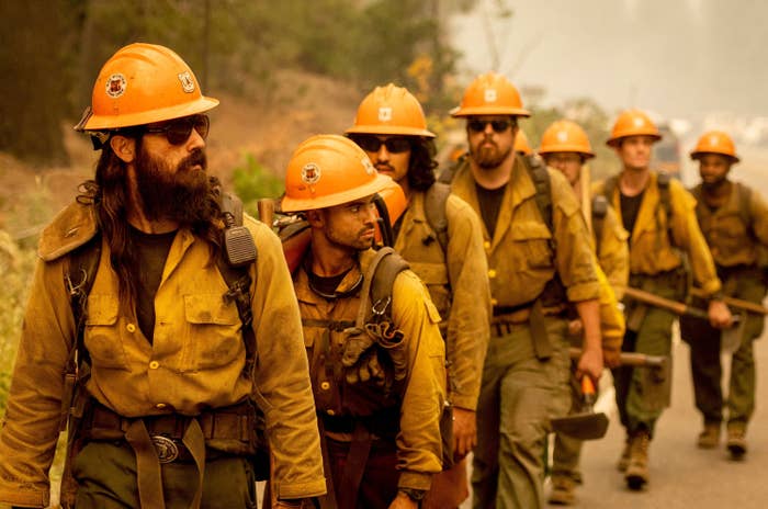 A line of firefighters wearing helmets and matching uniforms walking