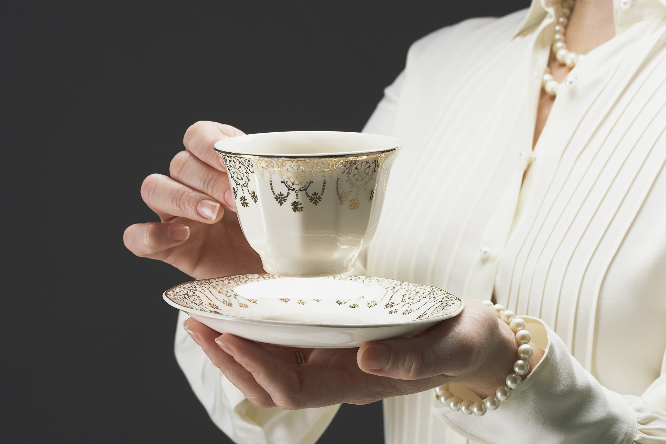 Person wearing a cardigan and a pearl bracelet holds a teacup and saucer