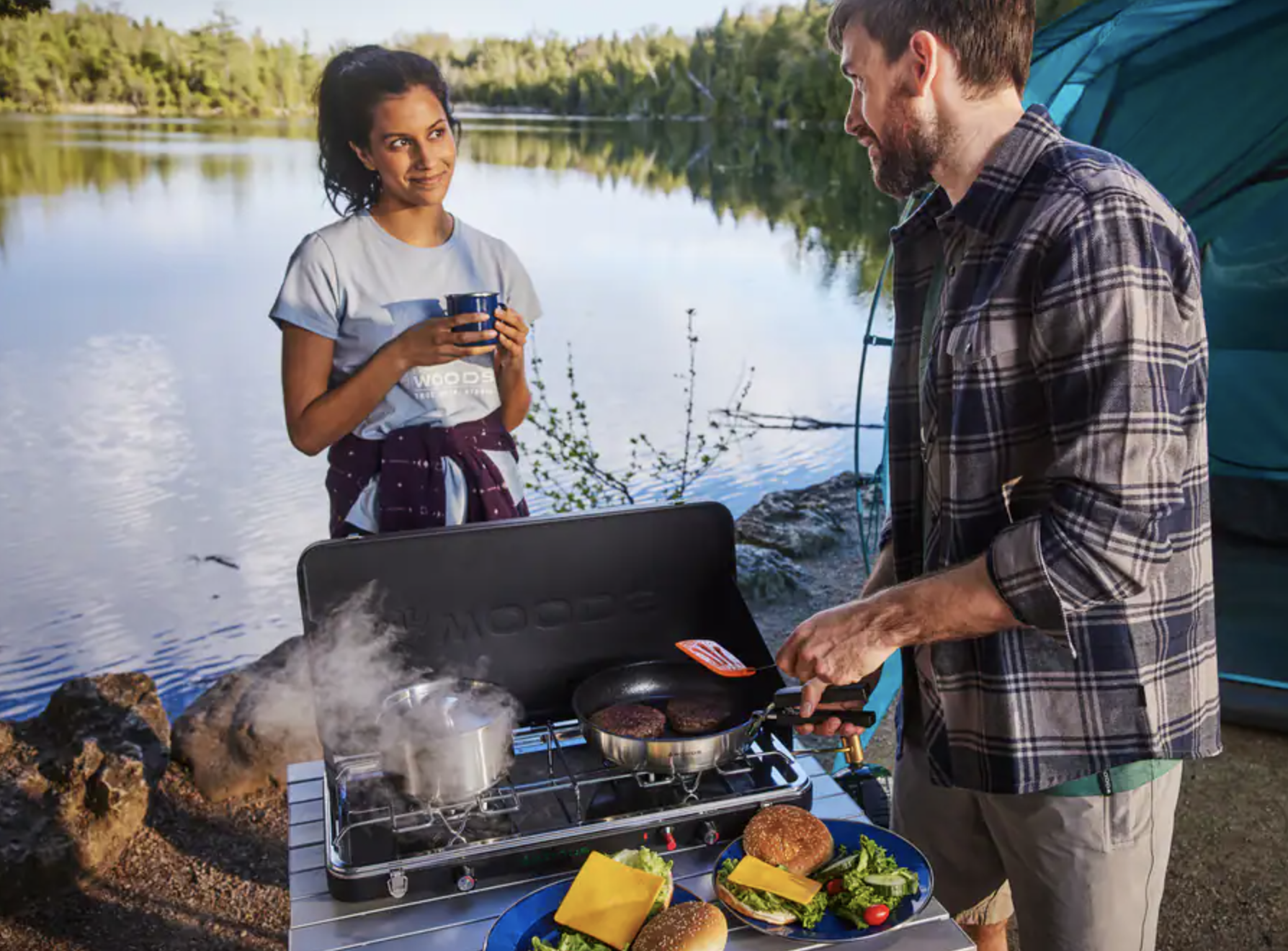 Two people chatting by a lake while cooking burgers on the stove