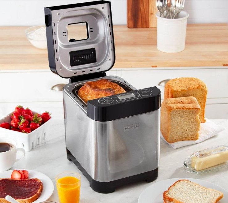 Baked bread in the bread maker next to a loaf of bread and various breakfast items