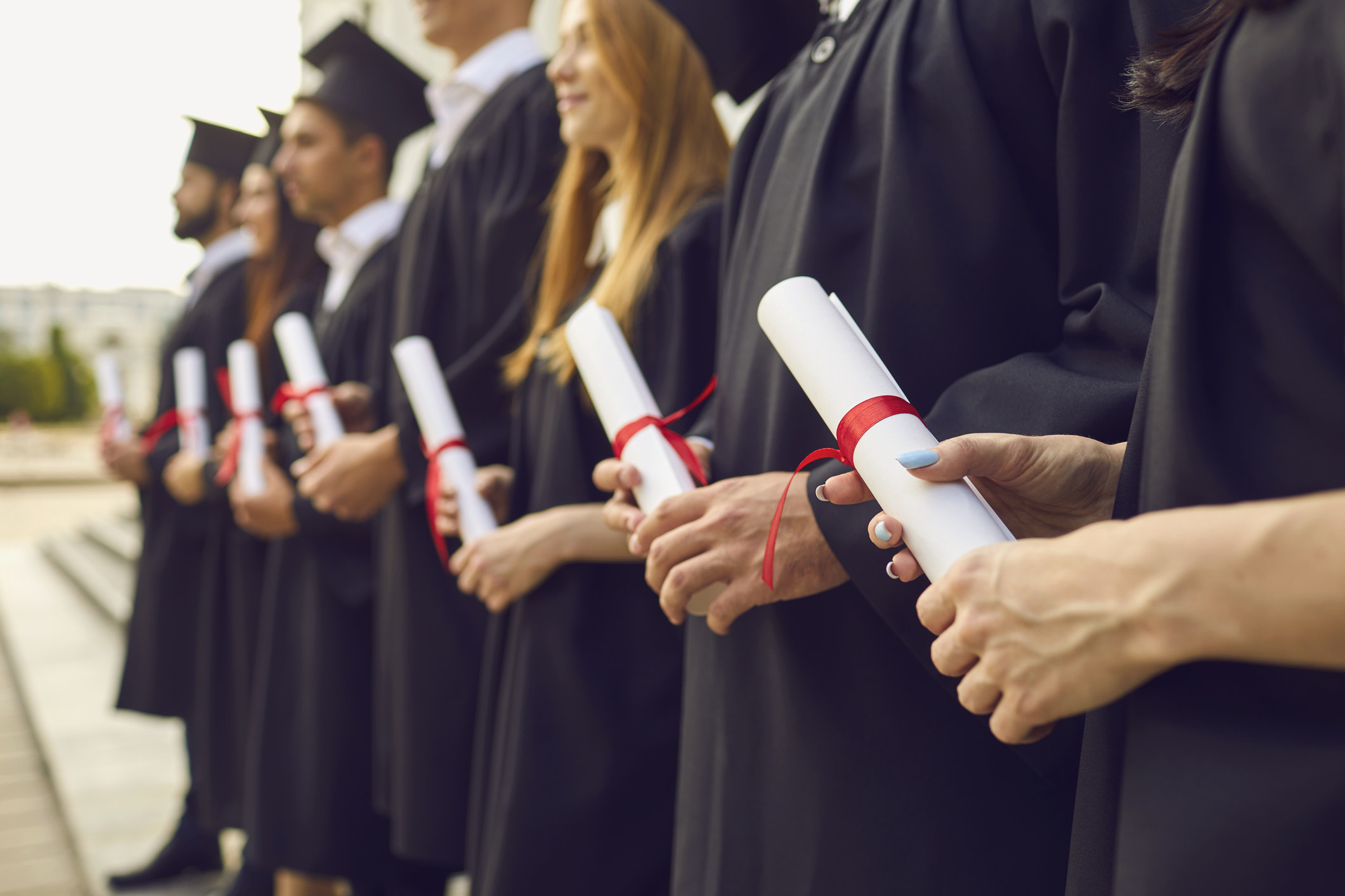 College grads holding their rolled-up diplomas