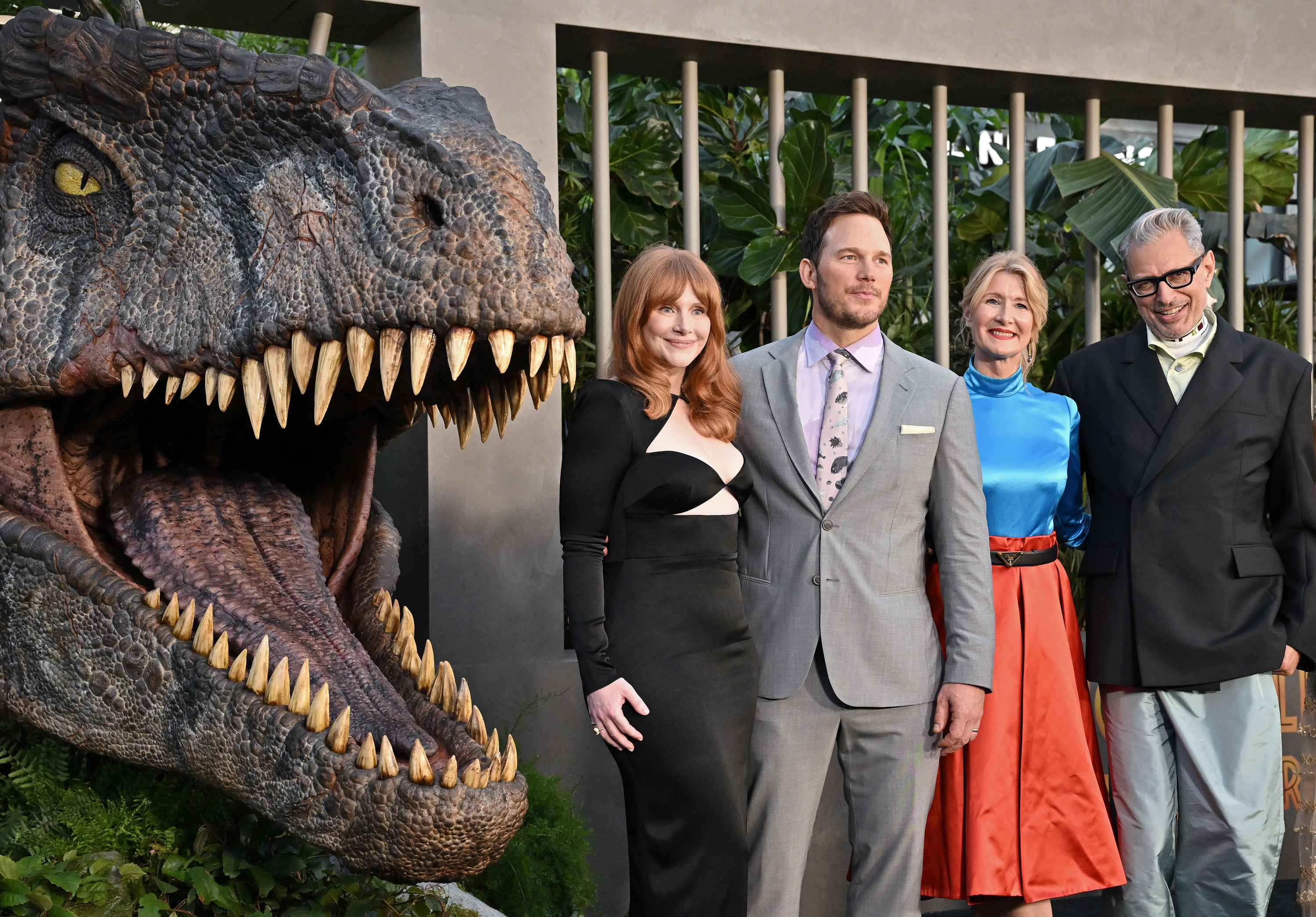 Chris Pratt, Bryce Dallas Howard, Laura Dern, and Jeff Goldblum on a red carpet standing in front of a giant dinosaur head